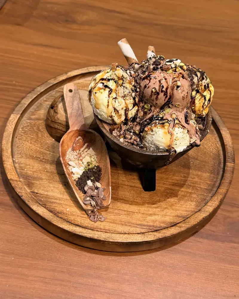 Six Wonders: scoops of ice cream with nuts and sauces in a dark footed bowl on a wooden tray